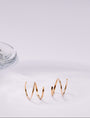 Gold double huggies on a white surface with a glass object in the background