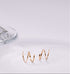 Gold double huggies on a white surface with a glass object in the background