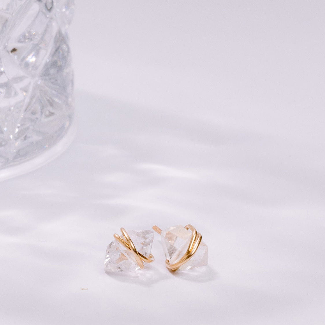 Clear glass earring with gold accent on a white marble surface