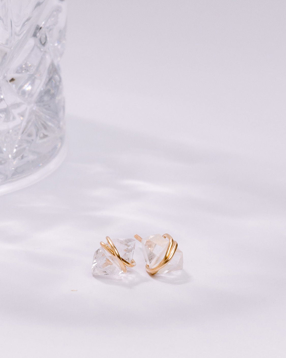 Clear glass earring with gold accent on a white marble surface