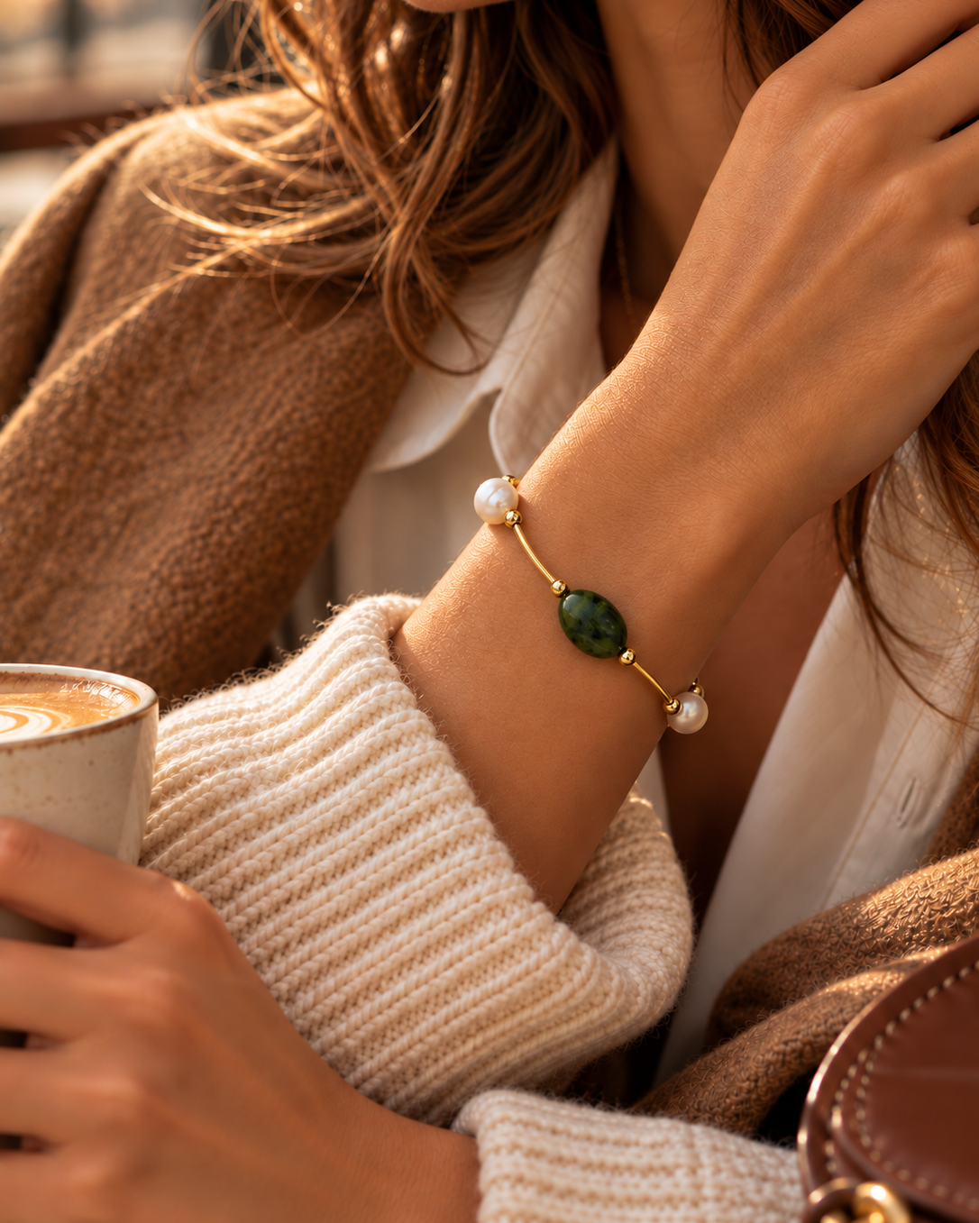 Girl in cafe wearing a cream sweater, tan jacket, brown hair and the Canadian green jade and pearl bracelet
