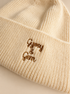 Close-up of a cream-colored ribbed knit beanie with brown embroidered text reading 'Gypsy & Gem' on the cuff.