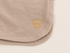 Close-up of a light beige sweatshorts, featuring a small gold embroidered geometric symbol on the lower right.