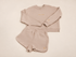 A two-piece women's loungewear set in a light beige or oatmeal color, consisting of a long-sleeve sweatshirt and matching shorts, laid flat on an ivory background