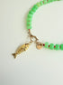 Close up of Green stone necklace with pink seed beads and a gold fish charm with a pink eye on a white background