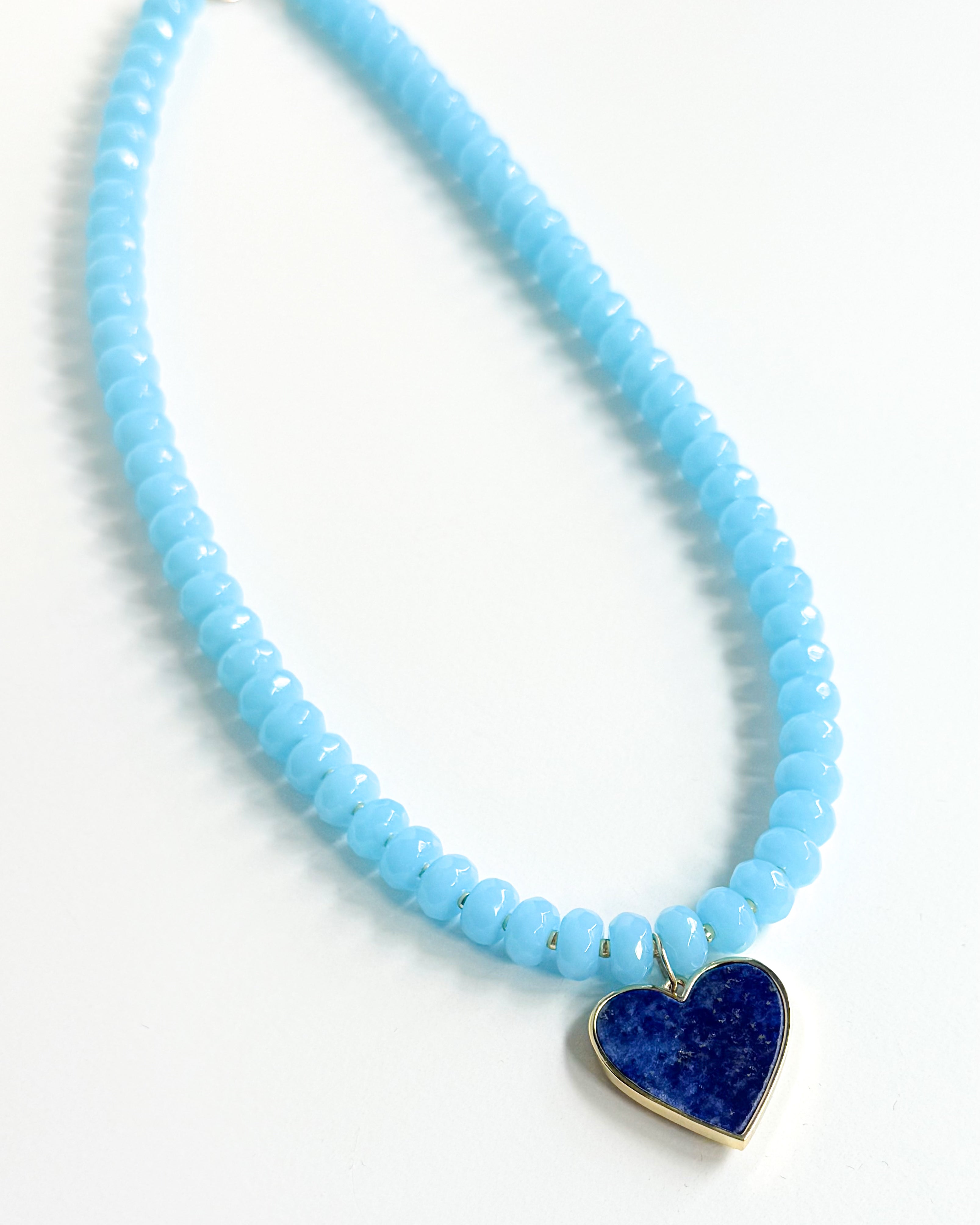 Necklace with light blue beads and a blue heart pendant on a white background