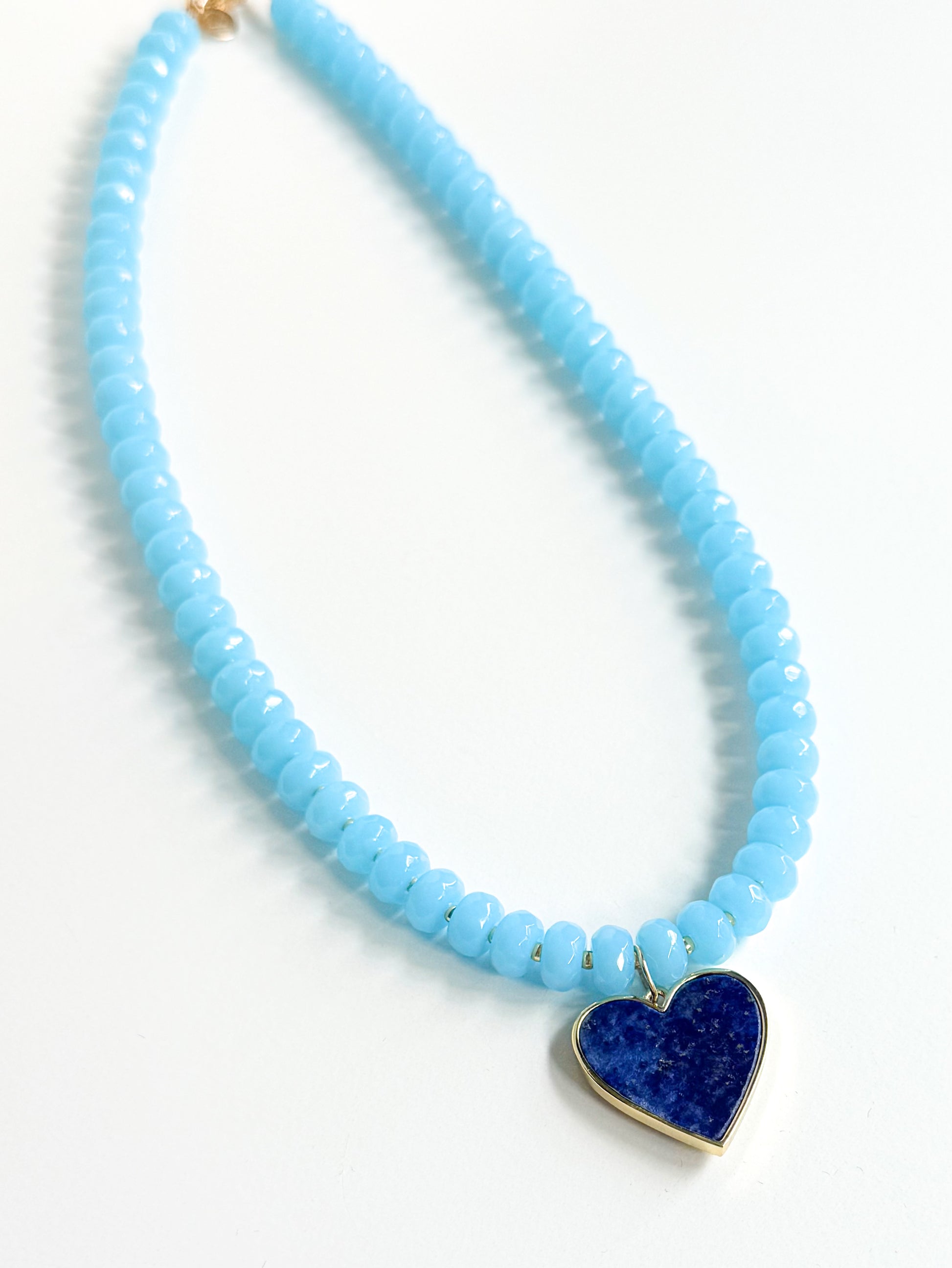 Necklace with light blue beads and a blue heart pendant on a white background