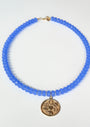 Blue beaded necklace with a gold pendant on a white background