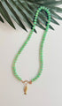 Green stone necklace with pink seed beads and a gold fish charm with a pink eye on a white background with a tropical leaf