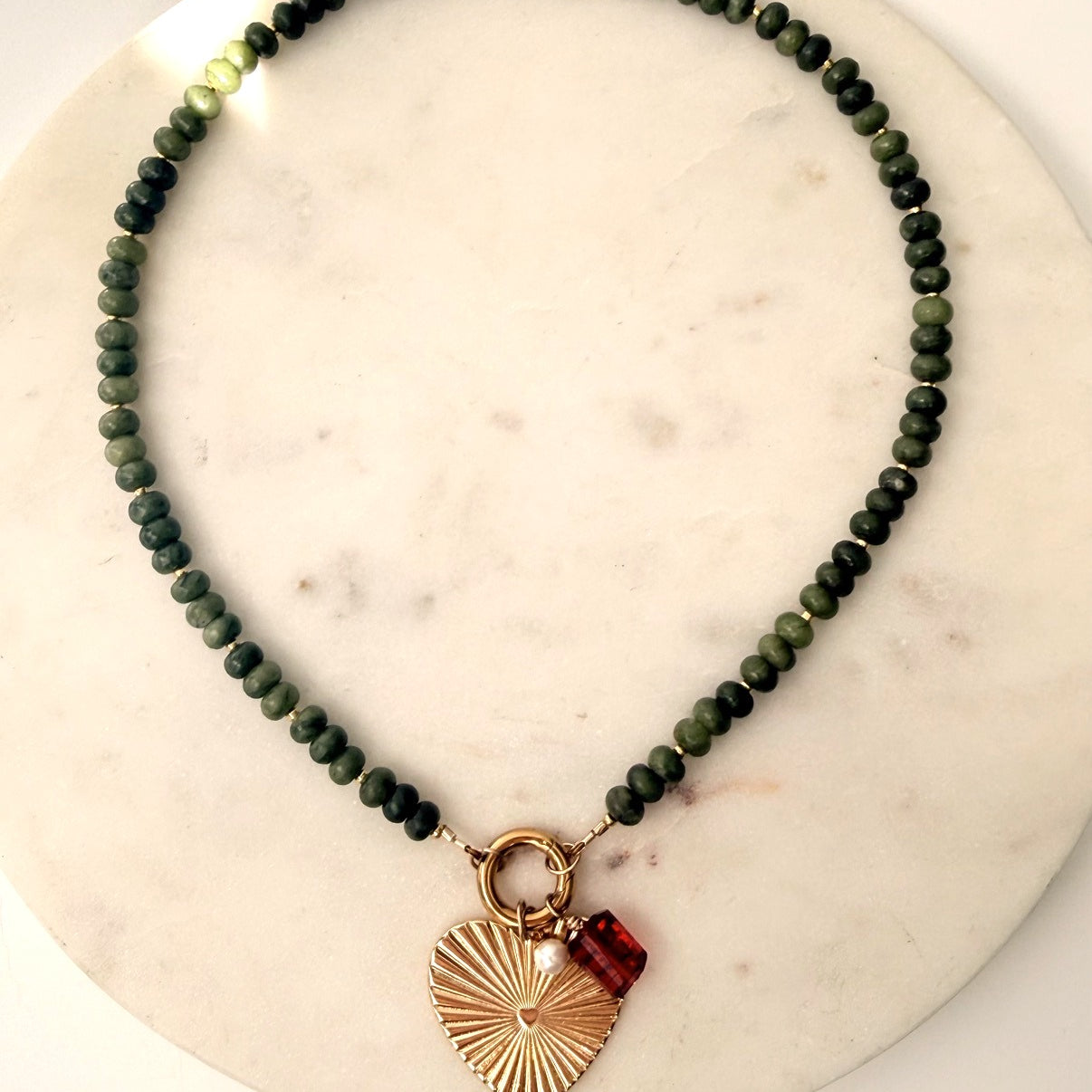 Green stone necklace with heart charm on a marble background