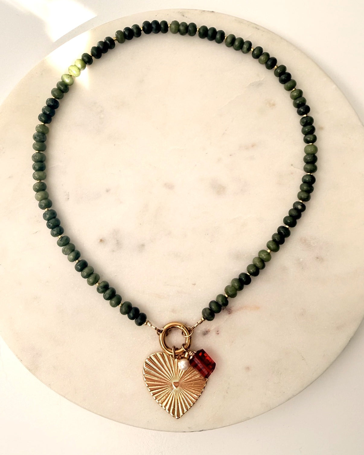 Green stone necklace with heart charm on a marble background