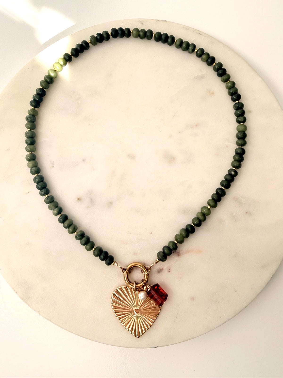 Green stone necklace with heart charm on a marble background