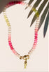 pink and green stone bead necklace with fish charm on white background with tropical leaf shadow