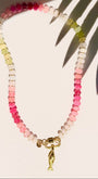 pink and green stone bead necklace with fish charm on white background with tropical leaf shadow