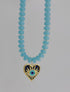 Showing movement and color detail of necklace with light blue beads and a heart-shaped pendant on a white background